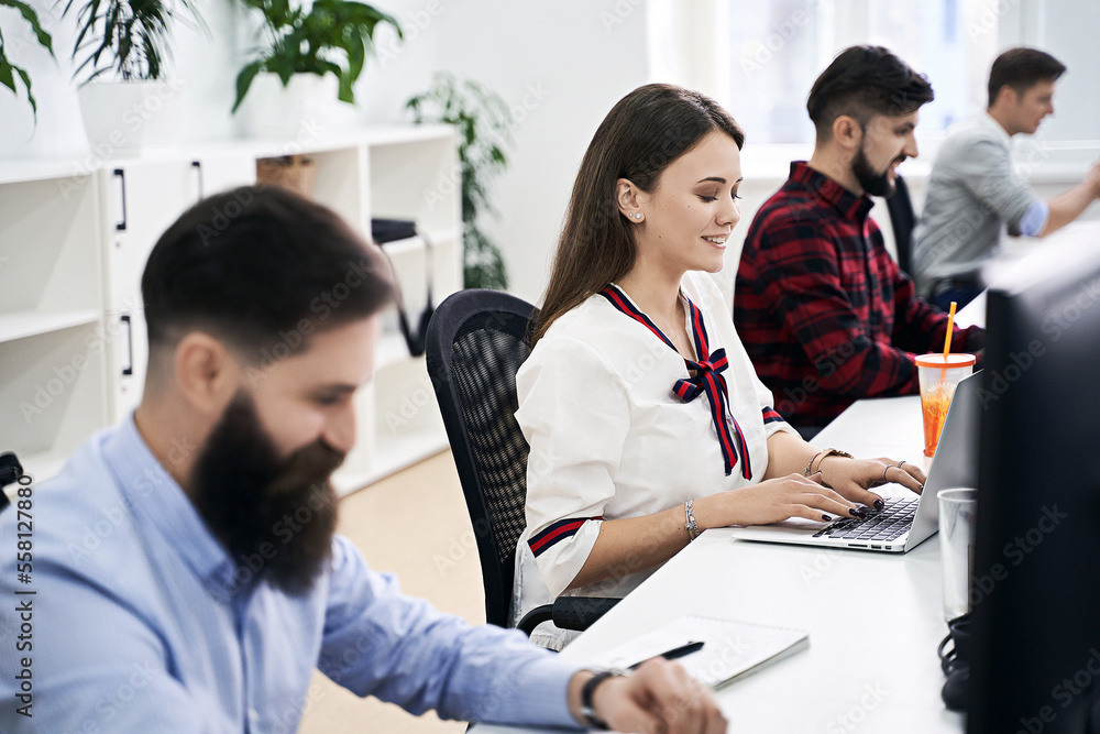 People working in modern IT office. Group of young and experienced programmers and software developers sitting at desks working on computers. Team at work. High quality image.