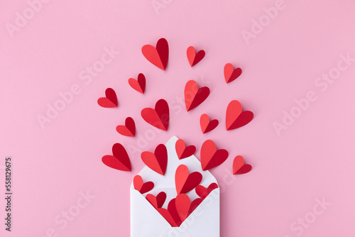 Saint Valentine day greeting card with love message. Envelope and paper red hearts on pink background top view. Flat lay.