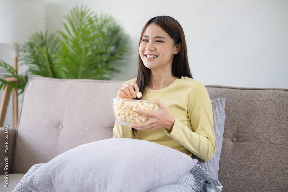Asian girl relaxing at home Enjoying Watching Television with glass bowl of popcorn