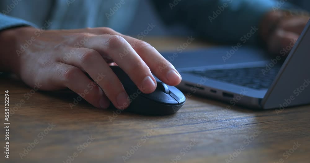 Close up of businessman is hold white computer mouse in hand and click. Man is working with laptop on wooden table. Male businessman is scrolling internet pages by mouse at workplace in office