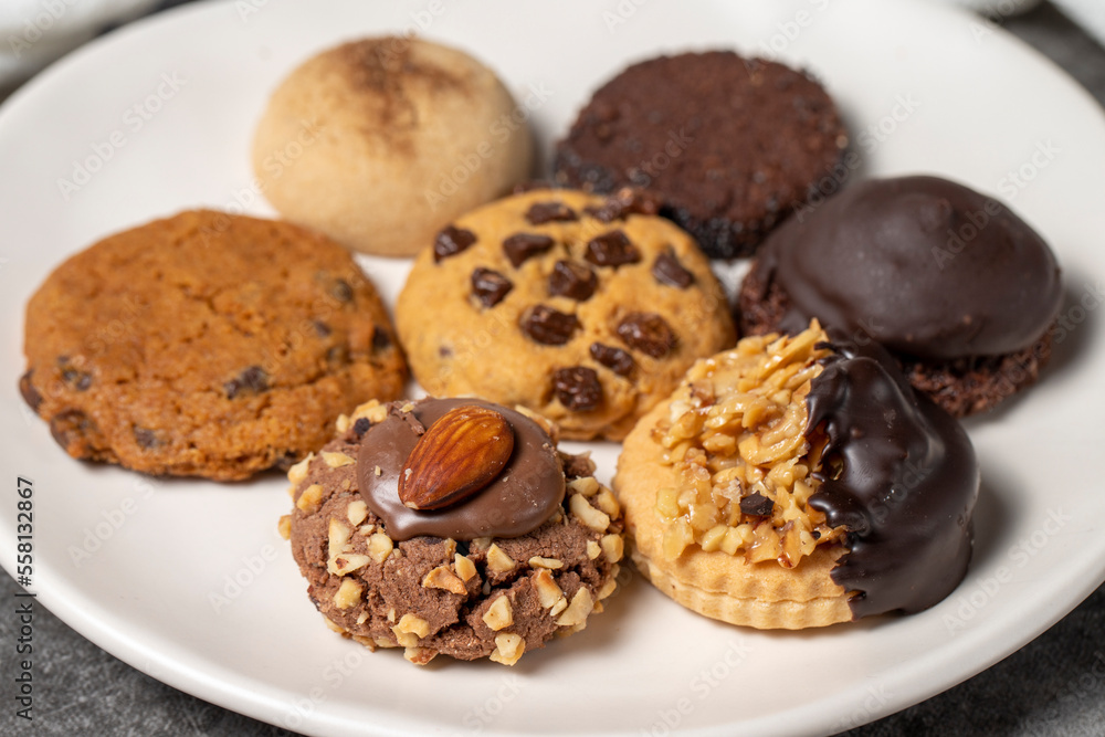 Sweet cookies on a dark background. Varieties of chocolate, hazelnut and pistachio cookies in a plate. close up
