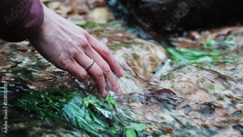 Hand of girl touches the water of a stream. Young hiker with ring wets his hand with cold water of a small mountain stream. Contact with nature, emotions and strong sensations.