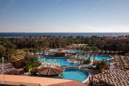 See from the top of the hotel. Beautiful palm trees. Mountains and sea. Roofs of houses. Sunny summer day. Colorful landscape.