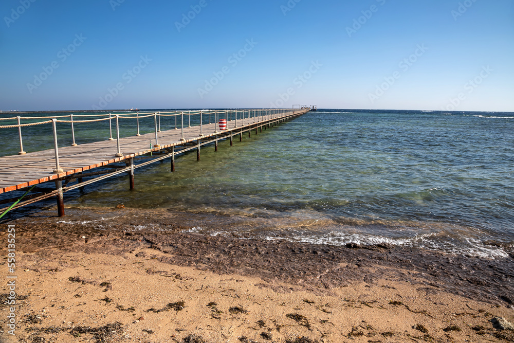Beautiful beach with a long pier. Yellow sand. Sunny summer day. Blue sky. Transparent beautiful sea.