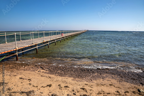 Beautiful beach with a long pier. Yellow sand. Sunny summer day. Blue sky. Transparent beautiful sea.