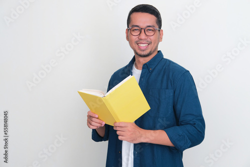 Adult Asian man smiling friendly at the camera while holding a book