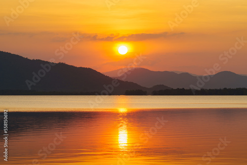 Silhouette, beautiful landscape with sunset at coast of the lake in summer. Nature twilight time, reflection, orange sky and yellow sunlight, romantic. Amazing scene at lake in Huai Mai Teng, Thailand