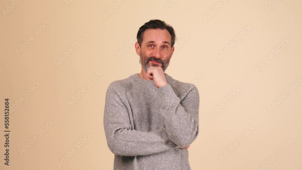 Serious adult bearded man wearing grey sweater disagrees with something in the beige studio Serious adult bearded man wearing grey sweater disagrees with something in the beige studio