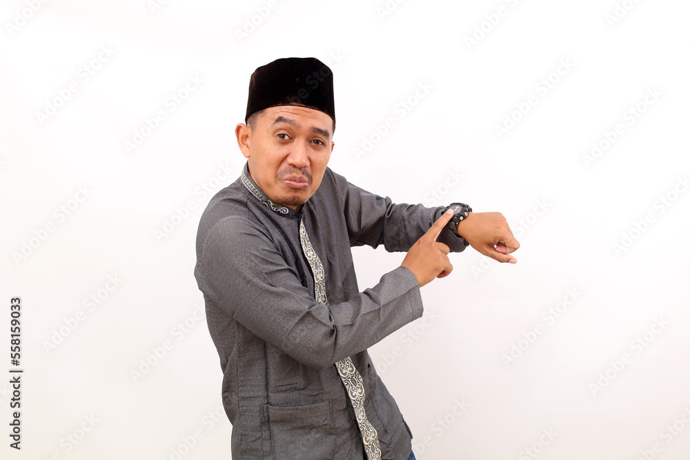 Asian muslim man standing while pointing on his watch. Isolated on white background Asian muslim man standing while pointing on his watch. Isolated on white background
