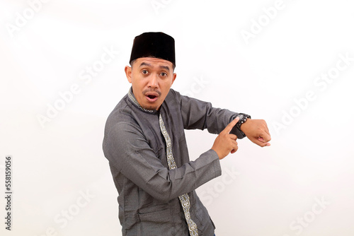 Asian muslim man standing while pointing on his watch. Isolated on white background photo
