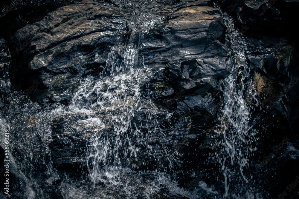 River stream flowing over the black rocks, water splashing on the rocks.