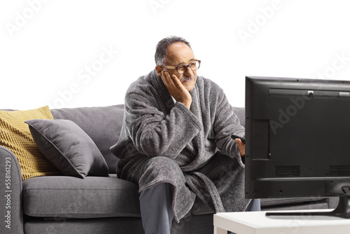 Bored mature man in a bathrobe, sitting on a sofa and watchin tv photo
