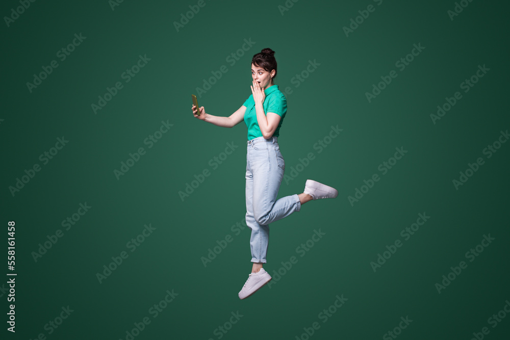 Full body profile photo of crazy ahocked woman jumping browsing telephone, isolated over green background. Mobile phone communication. Full body profile photo of crazy ahocked woman jumping browsing telephone, isolated over green background. Mobile phone communication.