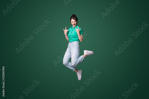Full body photo of crazy funky woman jump up in air making horned signs screaming isolated on green color background photo