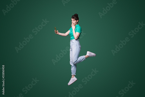 Full body profile photo of crazy ahocked woman jumping browsing telephone, isolated over green background. Mobile phone communication.