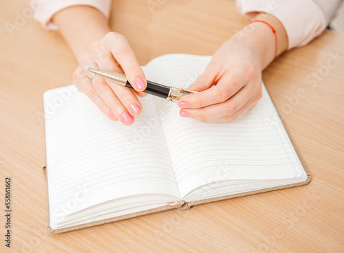 Close up of a woman's hands writing in a notepad placed on a wooden table, home office and work concept, plans and thoughts