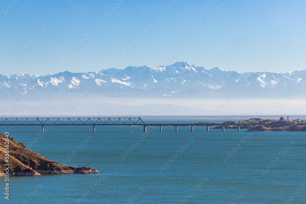 View of the Kapchagay reservoir with islands and a railway bridge against the backdrop of mountains in the Almaty region of Kazakhstan.