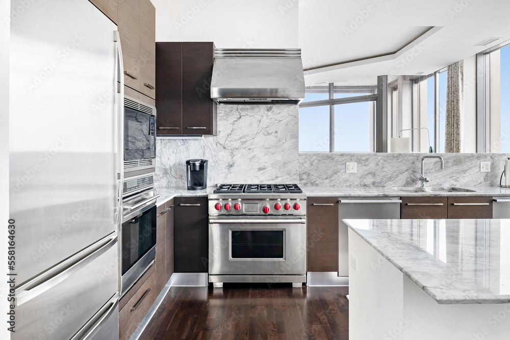 Modern Kitchen with Stainless Steel Luxury Appliances. Contemporary wood tone cabinets with white marble backsplash. Modern Kitchen with Stainless Steel Luxury Appliances. Contemporary wood tone cabinets with white marble backsplash.