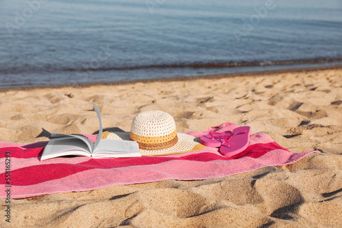 Beach towel with book, slippers and straw hat on sand near sea
