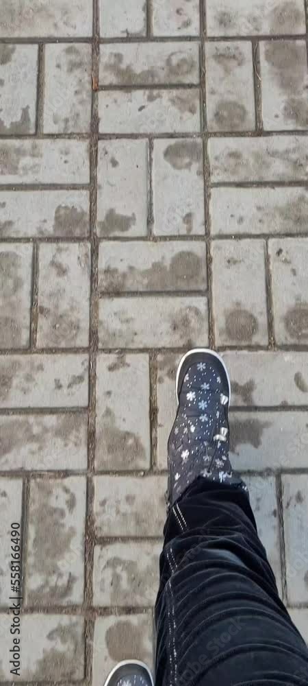Close up of a pair of winter shoes on a paving slabs background. Person walking on the pavement tile. Top view on the legs in warm black boots. Close up of a pair of winter shoes on a paving slabs background. Person walking on the pavement tile. Top view on the legs in warm black boots.