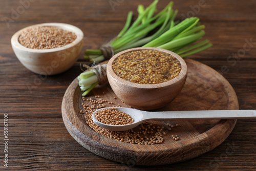 Tray with delicious whole grain mustard, seeds and fresh green onion on wooden table