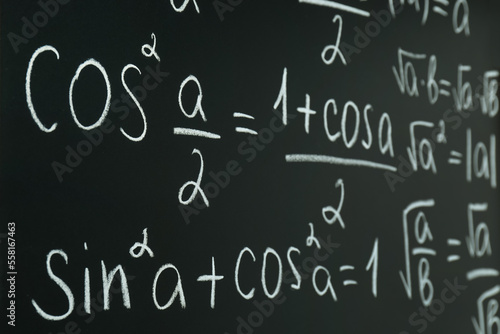 Different mathematical formulas written with chalk on blackboard  closeup