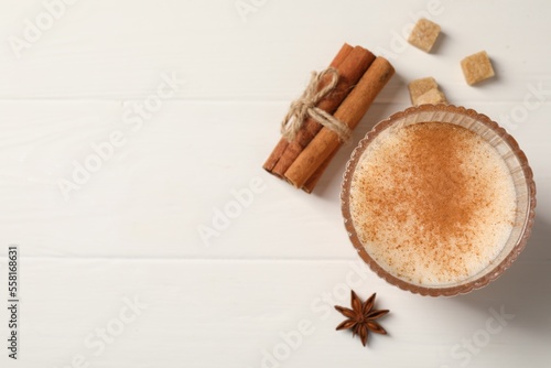 Delicious eggnog with anise and cinnamon on white wooden table, top view. Space for text