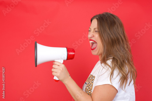 Young beautiful businesswoman with short blond hair standing over red studio background holding a speaker and shouting. Promotion and sales concept. 