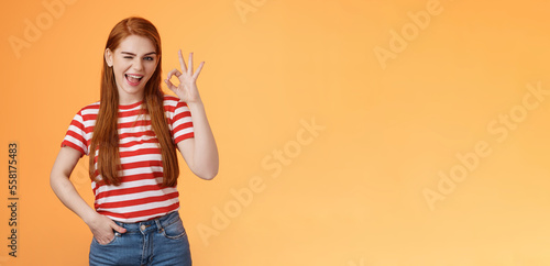 Sassy stylish sly redhead cheerful girl assuring everything excellent, show okay sign and wink cheeky, accept awesome idea, approve good job, express satifaction from positive result, like choice photo