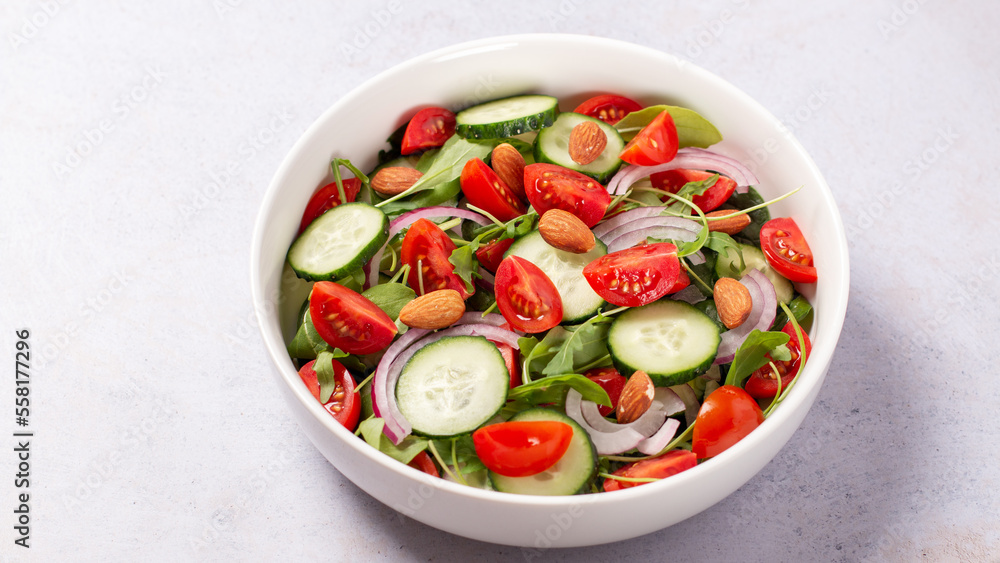Healthy salad with tomato, cucumber, greens and nuts on light background Healthy salad with tomato, cucumber, greens and nuts on light background