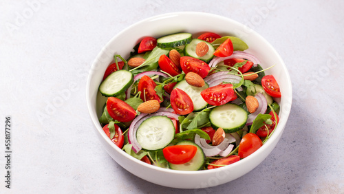 Healthy salad with tomato, cucumber, greens and nuts on light background