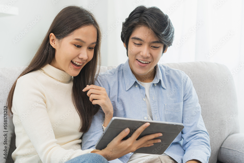 Happy excited, smiling asian young couple love using tablet pc, great deal or business success, received or getting cash back, tax refund, good news by mail while sitting on sofa, couch at home. Happy excited, smiling asian young couple love using tablet pc, great deal or business success, received or getting cash back, tax refund, good news by mail while sitting on sofa, couch at home.