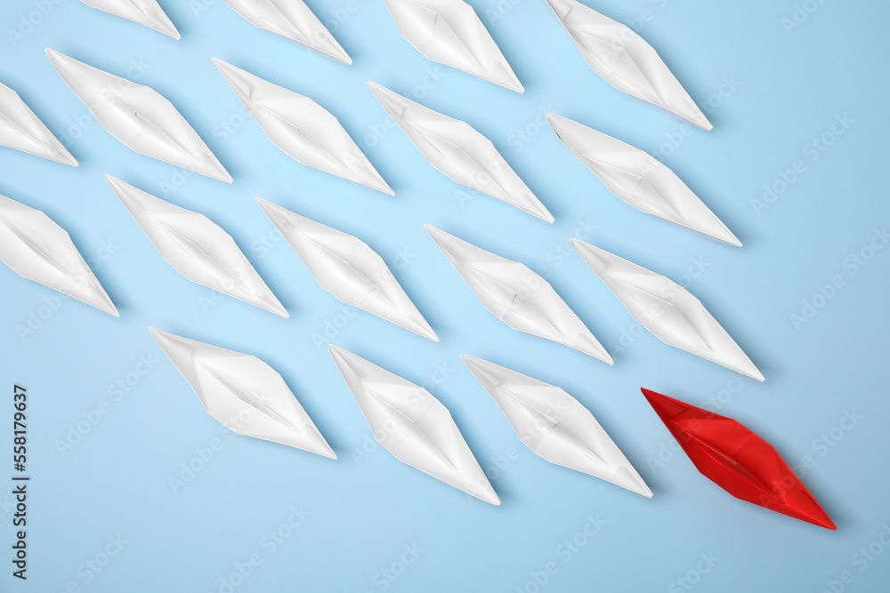 Obraz premium Paper boats following red one on light blue background, flat lay. Leadership concept