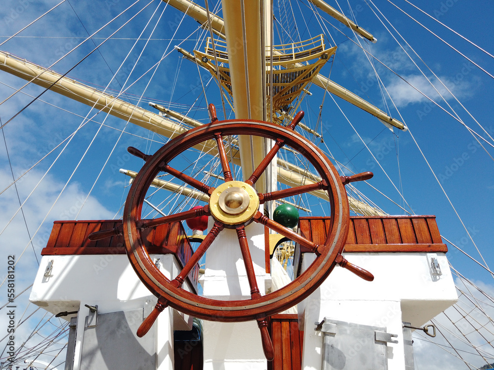 Ship wheel in front of masts and ropes