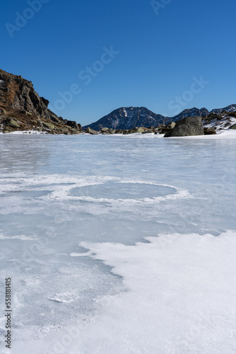 Vertical closeup shot of a frozen lake in the mountain during winter on a sunny day against a blue sky