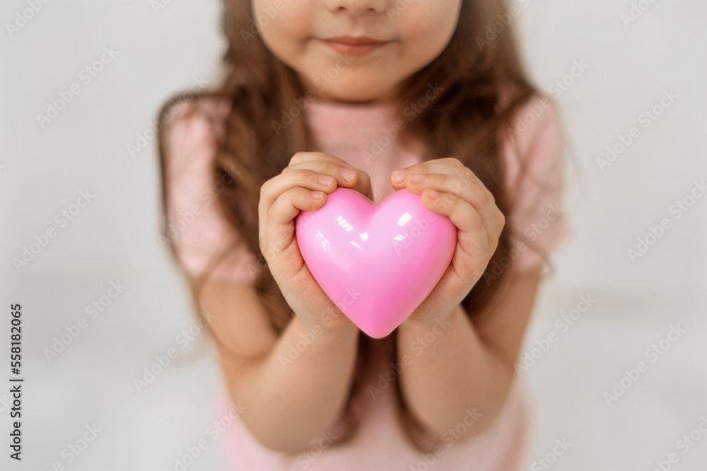 Little cute girl holds a pink heart in his hand stands on a white background. Copy space. Soft focus. Little cute girl holds a pink heart in his hand stands on a white background. Copy space. Soft focus.