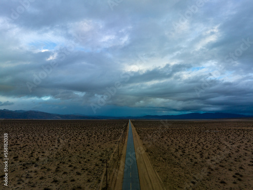 Desert road stretching into horizon under a vast sky with dramatic clouds at dusk, Mojave Desert