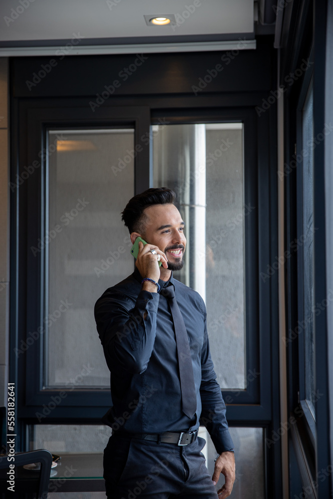 Handsome businessman in black suit talking on the phone in the office Handsome businessman in black suit talking on the phone in the office