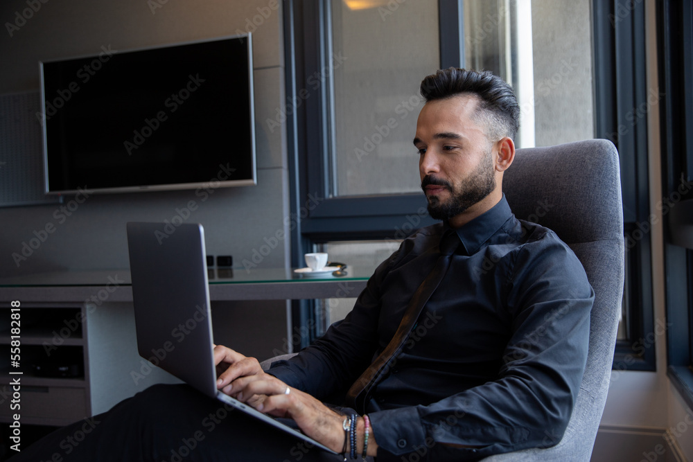 Man sitting with laptop on his lap, man in business suit in his suite accessing his computer Man sitting with laptop on his lap, man in business suit in his suite accessing his computer