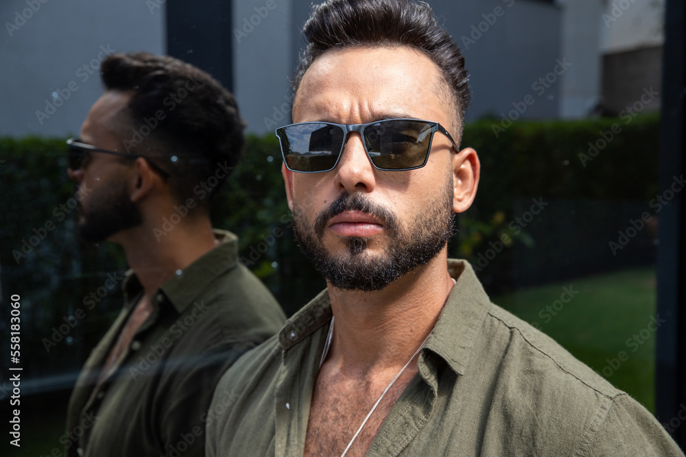 Obraz premium young bearded man wearing sunglasses looking at camera, photo taken outdoors, reflection appearing to the side, copy space