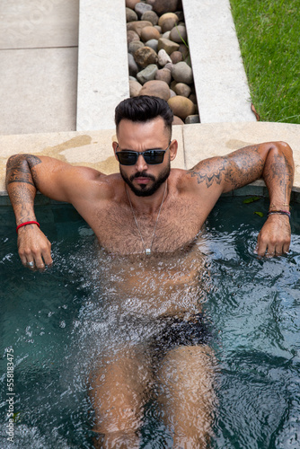 handsome muscular man in the pool, man with a beard, swimming trunks and tattoos in the water © VictorHugo