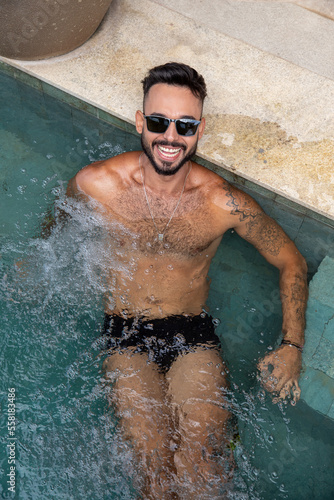handsome muscular man in the pool, man with a beard, swimming trunks and tattoos in the water