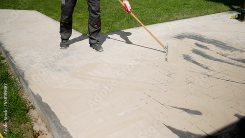 Pointing a patio with dry grouting cement grouting mix. Seeded fine sand on paving slabs - grouting. Sand with the help of the rule is rubbed into the seams of paving slabs. Grouting paving slabs.