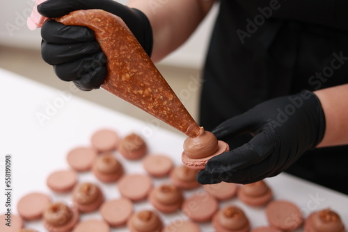 Canvas Print Close up of chef hands putting salt caramel with nuts in ganache cream on chocolate macarons shells