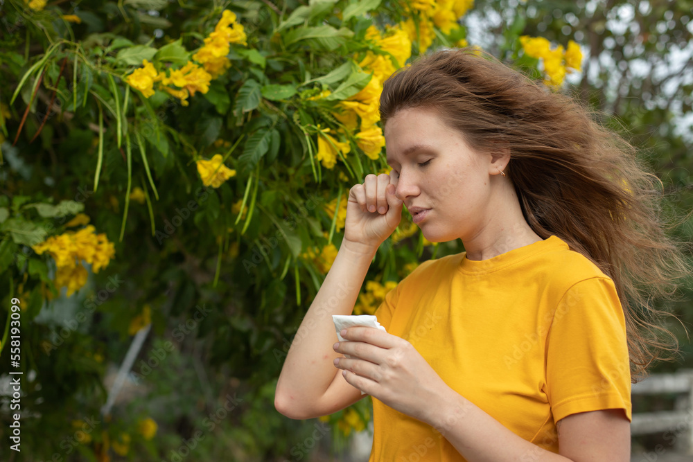 Portrait of beautiful young allergic woman is suffering from pollen allergy or cold on natural flower flowering tree background at spring or sunny summer day sneezes, blowing her runny nose rubs eyes Portrait of beautiful young allergic woman is suffering from pollen allergy or cold on natural flower flowering tree background at spring or sunny summer day sneezes, blowing her runny nose rubs eyes