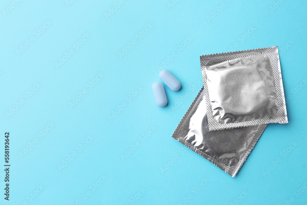 Pills and condoms on light blue background, flat lay with space for text. Potency problem Pills and condoms on light blue background, flat lay with space for text. Potency problem