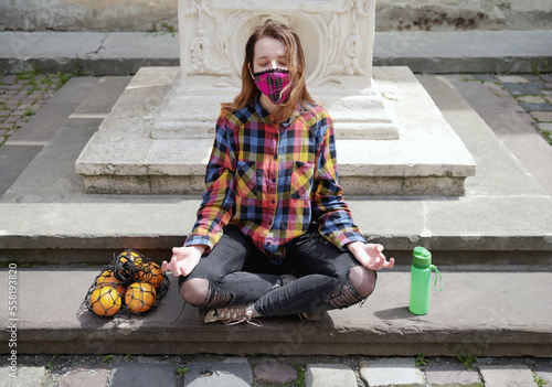 Obraz na płótnie Young female zero waster wearing a plaid handmade face mask medidates outdoor in the old city street w salonie