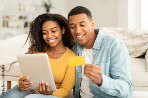 App for online shopping. Glad millennial african american guy hug lady, use tablet, credit card for order purchase