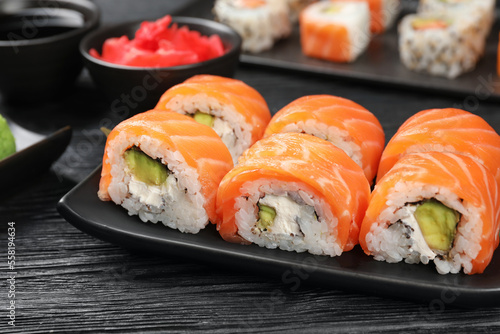 Tasty sushi rolls with salmon on black wooden table, closeup