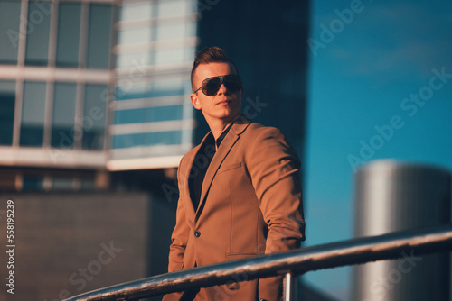 Serious handsome businessman man posing outdoor in brown suite and stylish sunglasses in the urbanistic area 